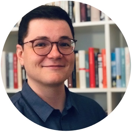 Autor Daniel Elias Junge steht lächelnd vor einem Bücherregal und blickt in die Kamera