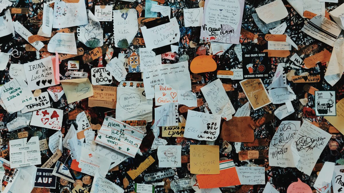 Mit schwarzem Edding vollgekritzelte Wand voller bunter Notizzettel und Post-its, auf denen die verschiedensten Dinge stehen.