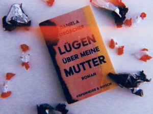Buch "Lügen über meine Mutter" von Daniela Dröscher auf einem weißen Tisch, umgeben von Süßigkeitenpapier